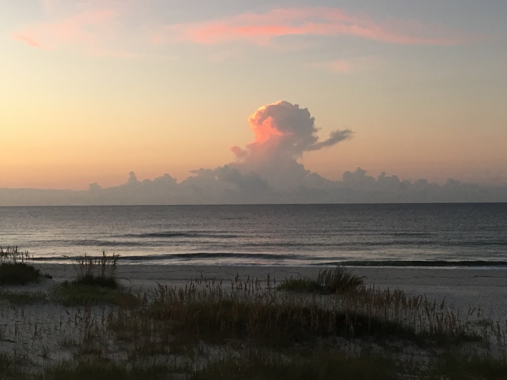 a sunset view of the ocean with a cloud in the sky