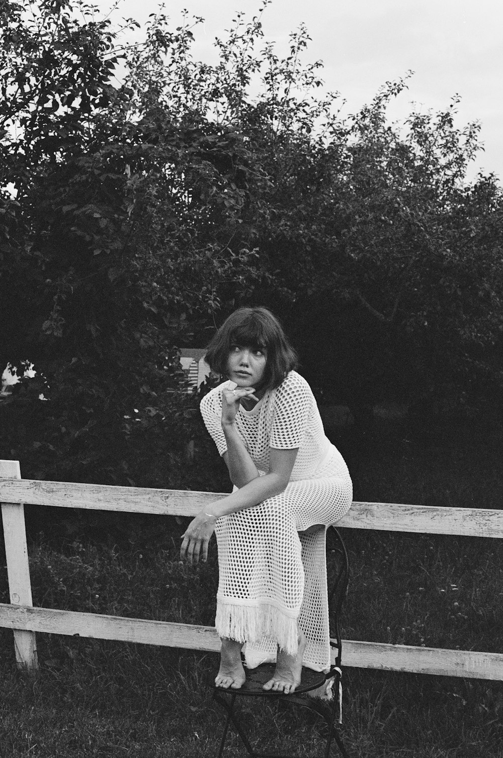 a black and white photo of a woman leaning on a fence