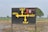 A black signboard with yellow directional arrows and text written in Punjabi, indicating directions to various locations. The sign includes the word 'Amul' and an image of an ice cream cone. The background shows a rural landscape with a field and some trees.