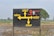 A black signboard with yellow directional arrows and text written in Punjabi, indicating directions to various locations. The sign includes the word 'Amul' and an image of an ice cream cone. The background shows a rural landscape with a field and some trees.