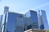 A group of modern skyscrapers with reflective glass facades, showcasing a blend of contemporary architecture. Some buildings have prominent logos visible on their surfaces.
