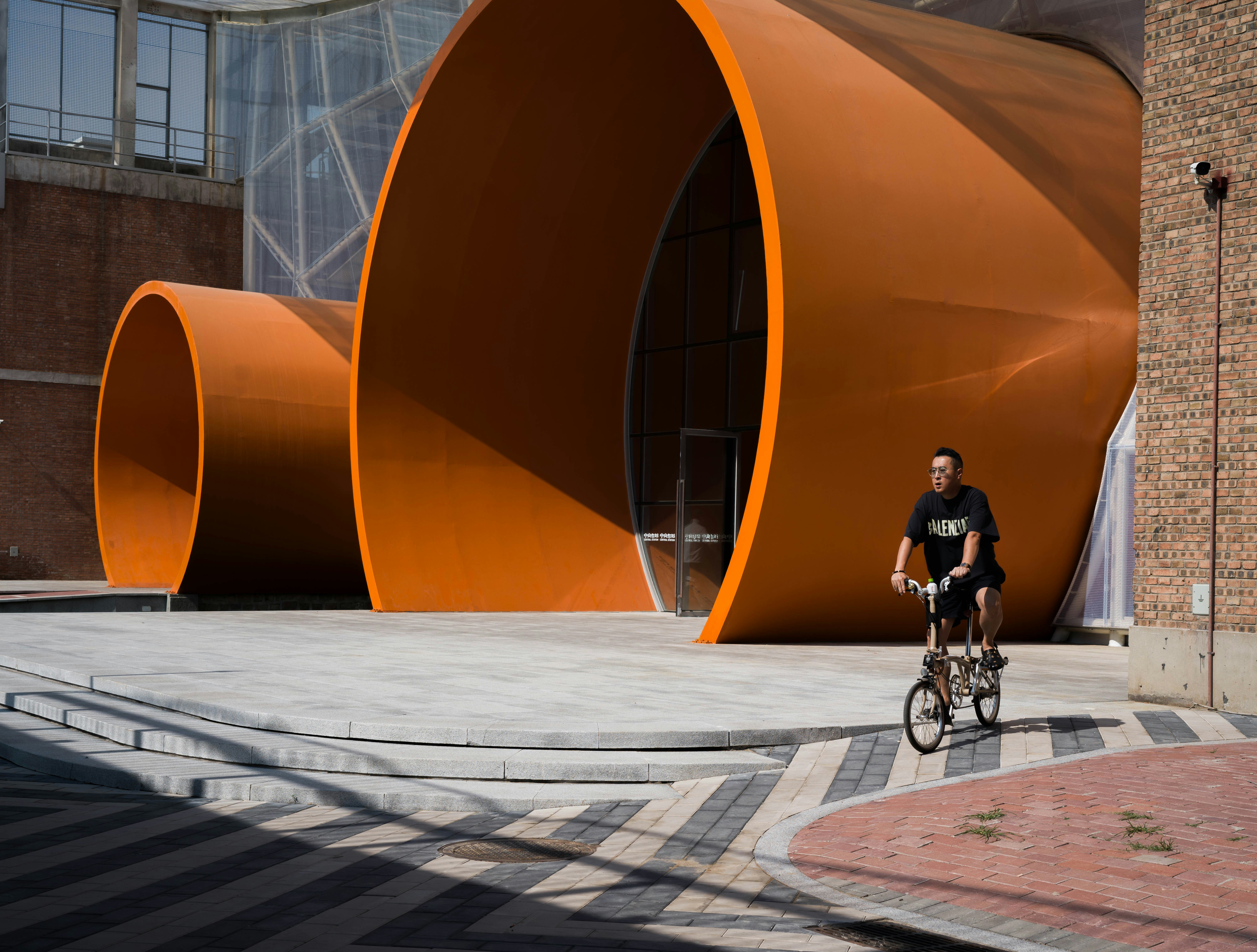 a man riding a bike past a large orange sculpture