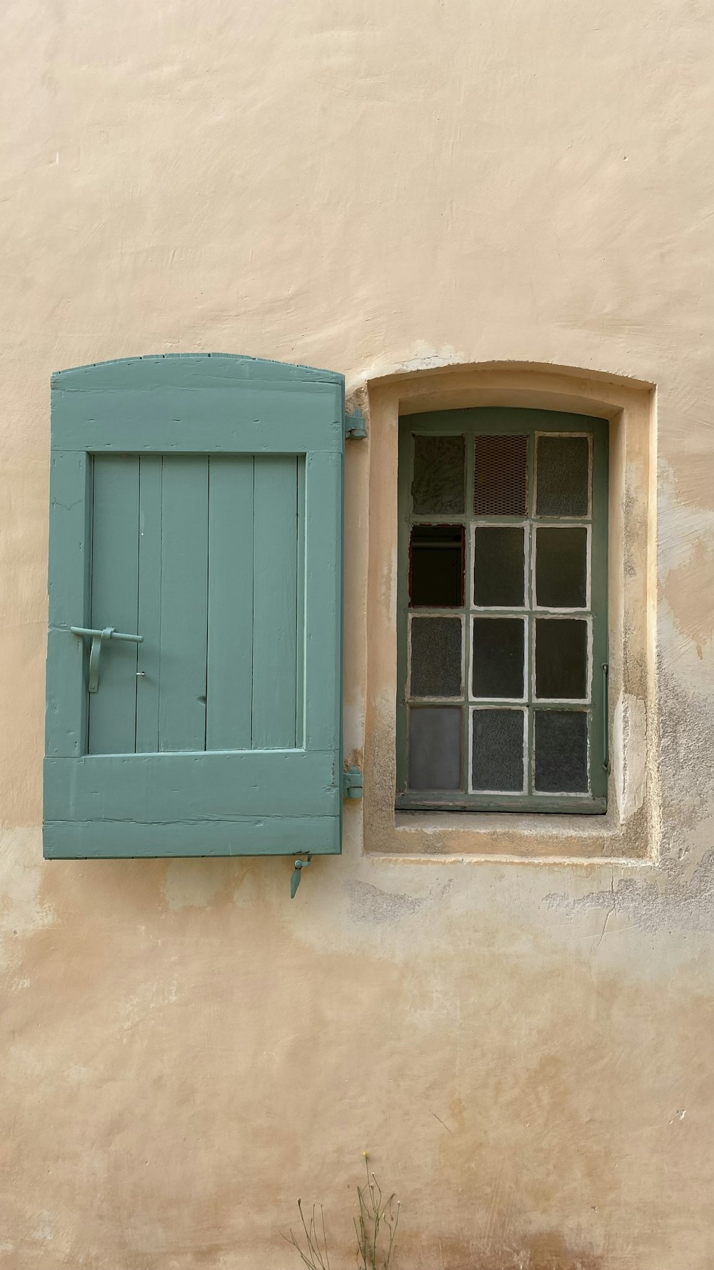 a window with a closed shutter and a cat sitting on the window sill