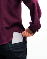 A person wearing a dark purple shirt and black pants is holding a small, rectangular notebook labeled 'Pocket Note' in their back pocket. The background is a simple, light color.