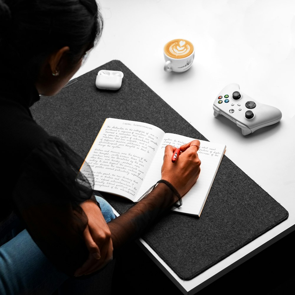 una persona seduta a un tavolo con un libro e un controller di gioco