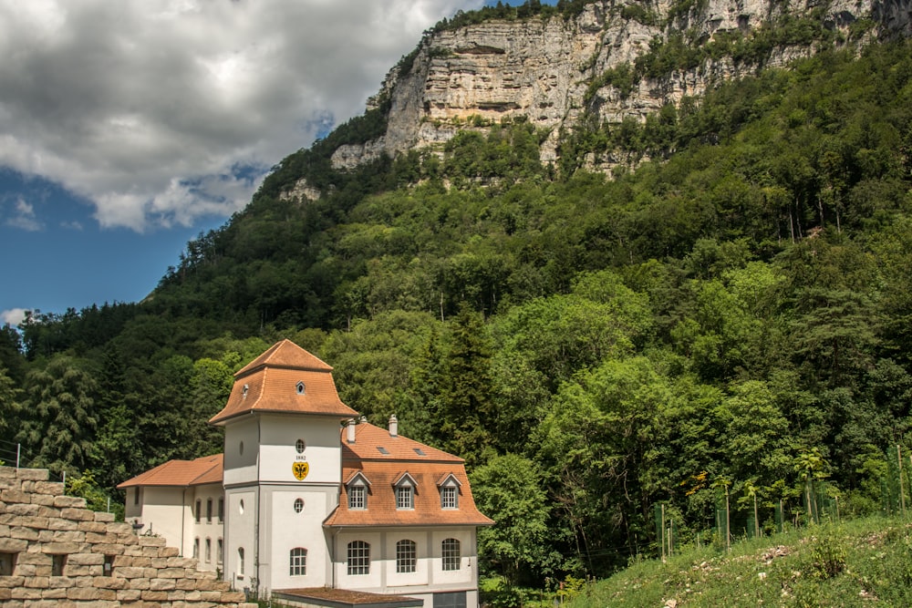 a white building with a red roof sitting in front of a lush green hillside