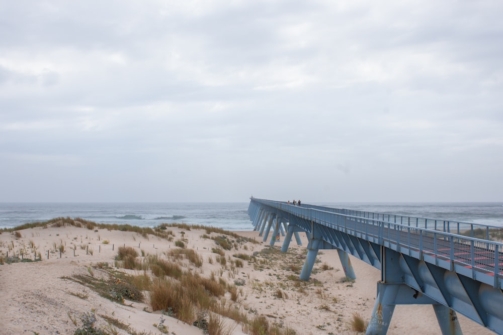 a blue bridge over a sandy beach next to the ocean