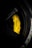 A close-up view of a yellow Nissan branded brake caliper with Brembo carbon ceramic labeling on a car wheel. The surrounding area includes parts of the black rim and tire with some branding visible. The lighting highlights the vibrant yellow of the brake caliper against the darker shades of the wheel.