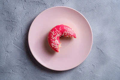 A close-up of a pastel pink squishy donut with colorful sprinkles, softly squeezed in a hand.