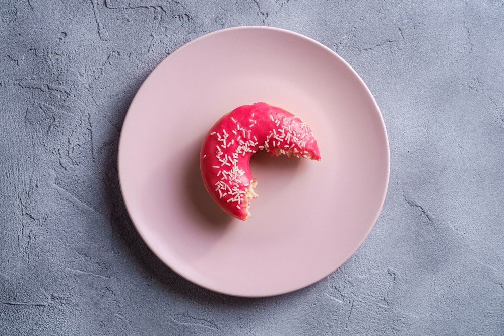 a pink plate with a half eaten donut on it