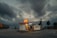 A solitary diesel gas station stands under a dramatic, overcast sky, suggesting an industrial setting. The lighting from the station contrasts with the dark clouds above, and a few trees are visible in the background. Cargo containers and industrial cranes can be seen in the distance, highlighting a dockyard ambiance.