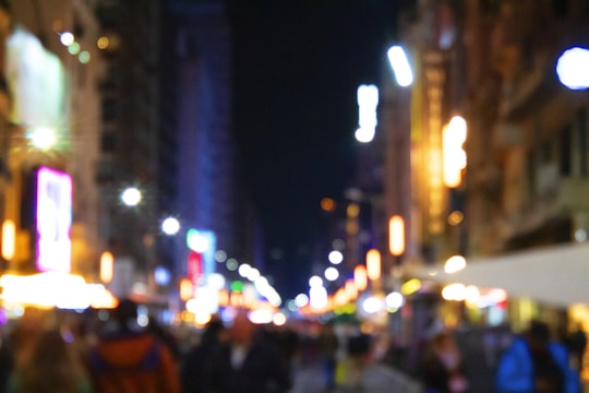 Nighttime city street with glowing neon signs and blurred motion of people walking.