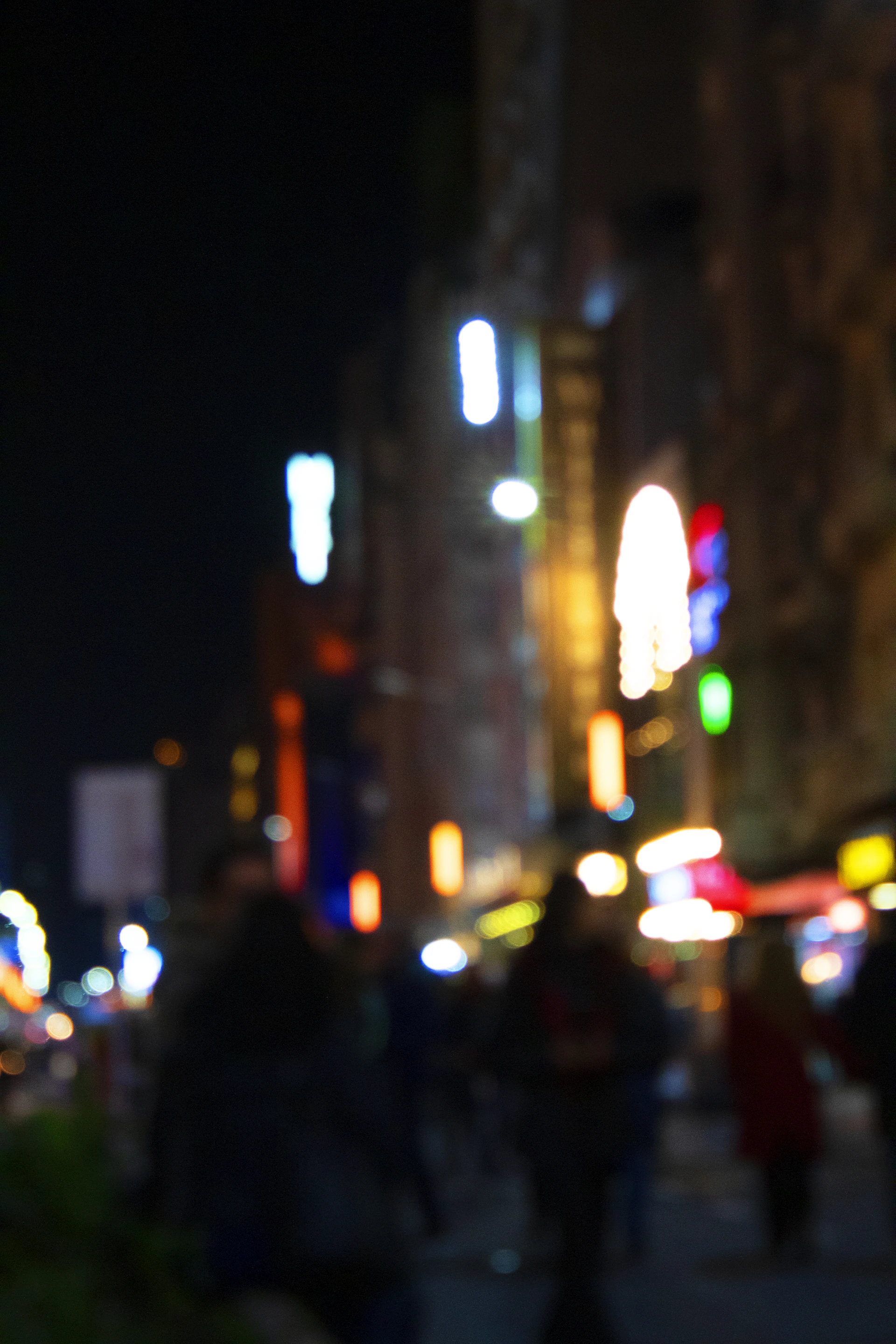 A candid moment of a city street at night, with blurred lights and people walking, reflecting the pulse of urban adventure.