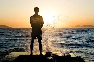 a man standing on top of a rock next to the ocean