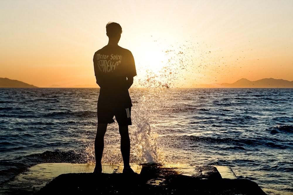 a man standing on top of a rock next to the ocean