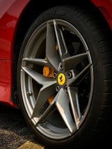 A close-up view of a car's wheel featuring a stylish alloy rim with a distinctive yellow emblem at its center. The tire is marked with 'ZERO' and appears to be part of a high-performance vehicle. The car's body is painted in a glossy red color, partially visible next to the wheel.