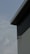 A security camera is mounted on the corner of an industrial-style building with corrugated metal siding. The view focuses on the building's geometric lines, contrasting with a cloudy sky in the background.