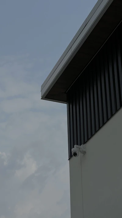 A close-up of a sleek security camera mounted on a modern office building corner during sunset.