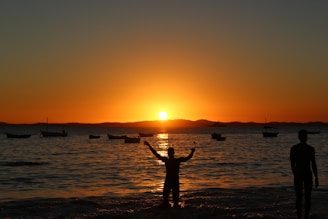 two people standing on a beach at sunset