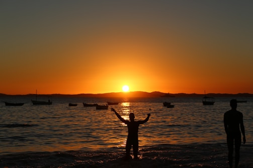 two people standing on a beach at sunset