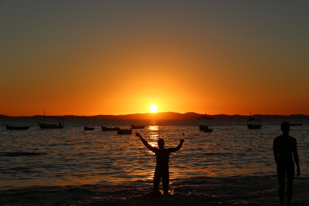 two people standing on a beach at sunset