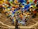 A stunning ceiling installation featuring a multitude of colorful glass flowers in various shapes and sizes. The floral elements create a vibrant and dynamic display that resembles a blooming garden. The setting is a grand indoor space with elegant architectural details and soft lighting.