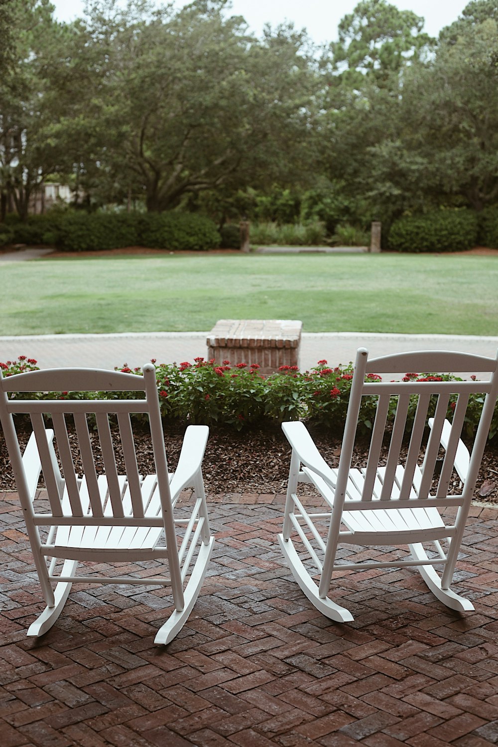 a couple of white rocking chairs sitting on top of a brick patio