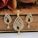 A gold pendant with matching earrings, intricately designed with teardrop shapes adorned with small, sparkling stones. The jewelry set rests against a wooden background, with delicate chains and clasps visible. The shine and elegance of the pieces suggest they are crafted for special occasions.