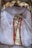 A statue or idol adorned in gold and red attire is surrounded by an ornate, gold and white decorative frame. The fabric draped around the figure adds a sense of elegance and sanctity.