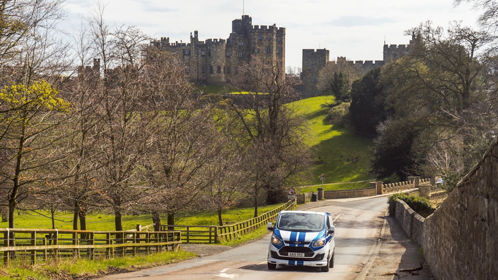 a blue and white car driving down a road in front of a castle