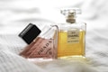 Two elegant perfume bottles are displayed on a soft, textured fabric surface. One bottle, labeled Prada, is tilted and has a light pink hue, while the other, labeled Chanel No 5, is upright with a golden yellow liquid inside. The scene exudes luxury and sophistication.