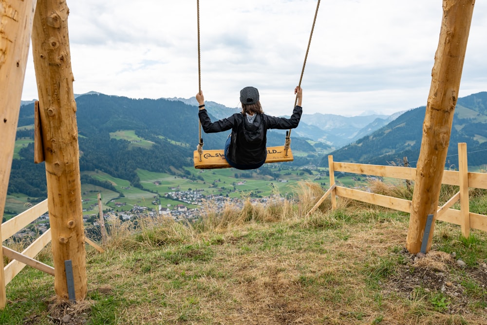 a person in a black jacket is swinging on a wooden swing