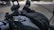 A close-up of a motorcycle's handlebar area showing the mounting bracket for an accessory. The background is blurred, indicating a shallow depth of field.