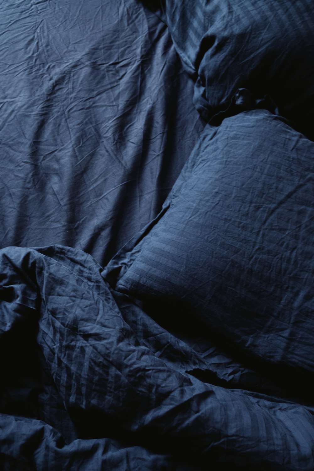 an unmade bed with blue sheets and pillows