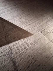 A concrete surface with a textured finish is partially illuminated by light, creating a triangular shadow alongside grainy textures and scattered small holes.