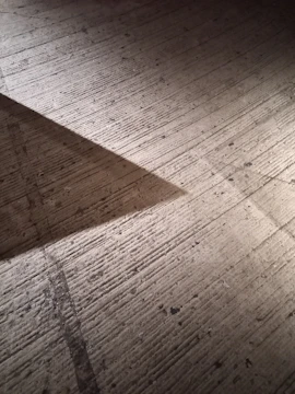 A concrete surface with a textured finish is partially illuminated by light, creating a triangular shadow alongside grainy textures and scattered small holes.