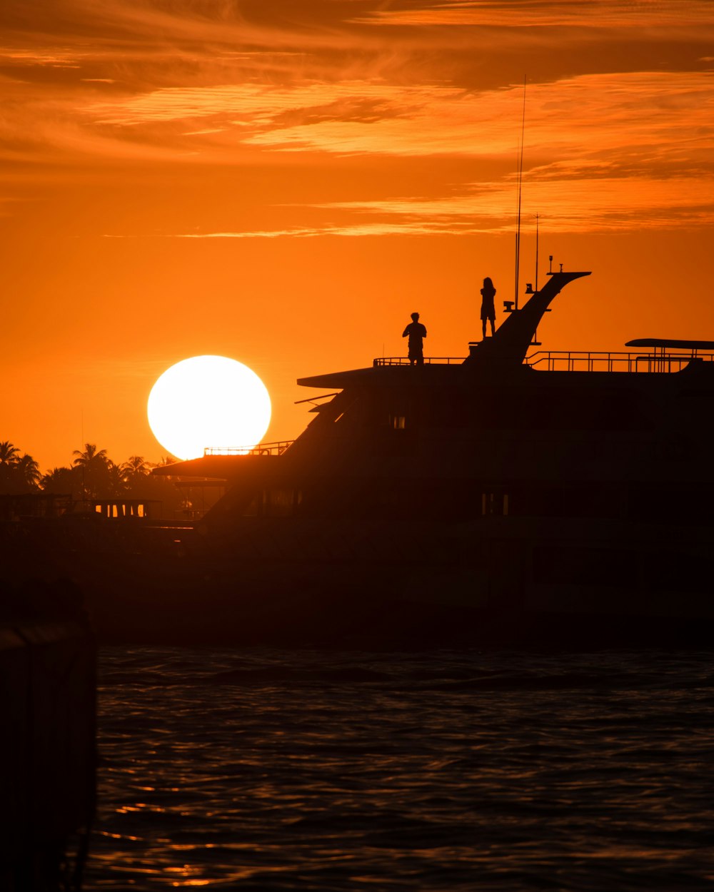 two people standing on the roof of a boat at sunset