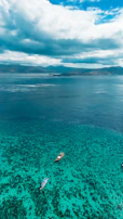 Colorful boats bobbing gently near a vibrant coral reef under a bright blue sky.