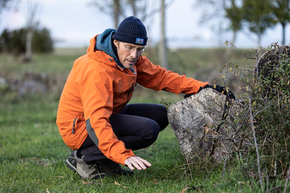 a man in an orange jacket leaning on a rock