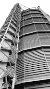A towering industrial structure with large, horizontal slats and a series of interconnected metal staircases and platforms running vertically along the side. It features a robust, geometric design.