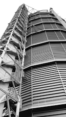 A towering industrial structure with large, horizontal slats and a series of interconnected metal staircases and platforms running vertically along the side. It features a robust, geometric design.