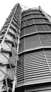 A towering industrial structure with large, horizontal slats and a series of interconnected metal staircases and platforms running vertically along the side. It features a robust, geometric design.
