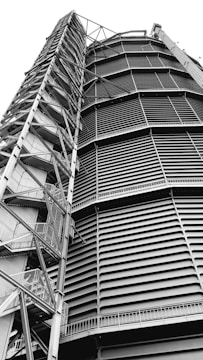 A towering industrial structure with large, horizontal slats and a series of interconnected metal staircases and platforms running vertically along the side. It features a robust, geometric design.