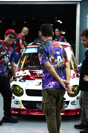 A group of friends wearing different custom car shirts, standing by their vintage cars.