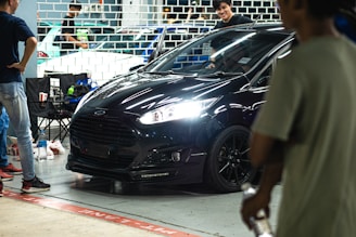 A friendly Vanta Auto team member shaking hands with a happy customer beside a sleek black car.