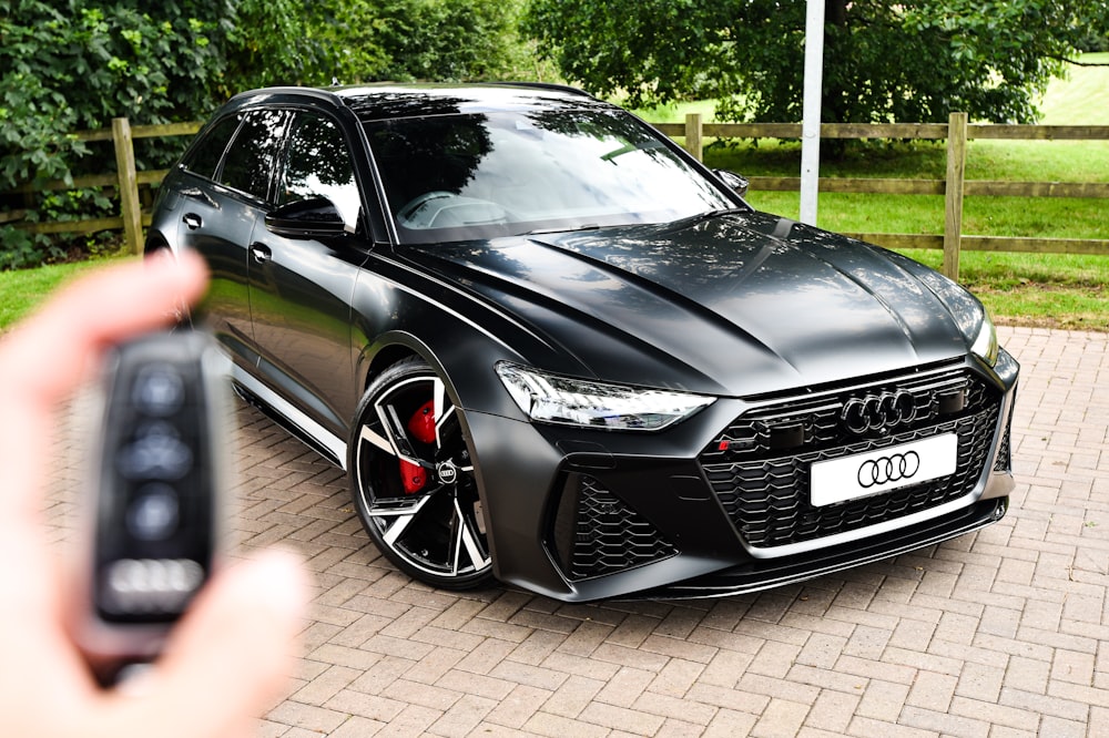 a person holding a cell phone in front of a black car