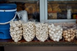 Several bags filled with popcorn and various snacks are displayed on a counter. A blue cooler with a white lid and handle is positioned to the left. In the background, there are more snacks and plastic cups visible through a window.