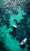 An aerial view of turquoise waters with boats casting shadows below.