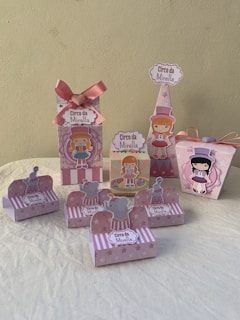 A collection of decorative party favor boxes with a circus theme featuring cartoon characters. They are adorned with images of girls in circus attire and small elephants wearing hats. The boxes are primarily pink with accents of white and light purple, some featuring star patterns. A large pink bow is prominent on one of the boxes.