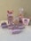 A collection of decorative party favor boxes with a circus theme featuring cartoon characters. They are adorned with images of girls in circus attire and small elephants wearing hats. The boxes are primarily pink with accents of white and light purple, some featuring star patterns. A large pink bow is prominent on one of the boxes.